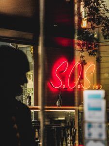 Neon sign hanging in a store front window that says "S.O.S..."